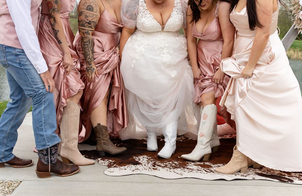 Wedding party showing coordinated boots, bride in white cowboy boots surrounded by bridesmaids in pink dresses.