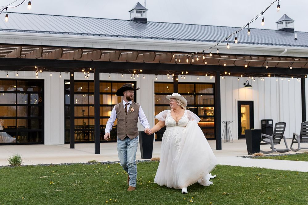 Bride and groom holding hands walking outside rustic barn wedding venue with string lights.