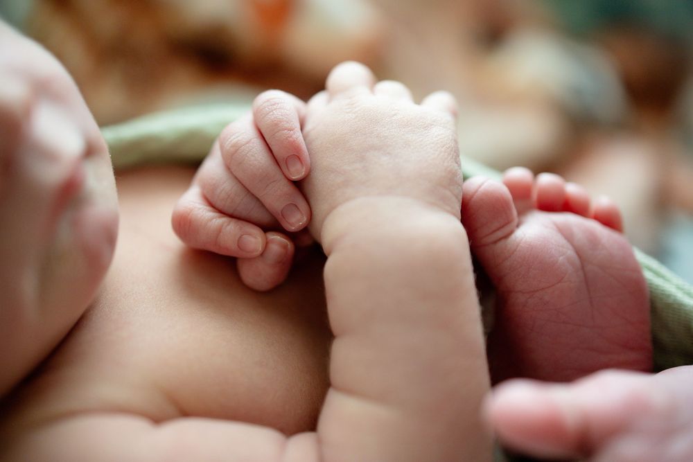 Close-up of newborn baby tiny fingers and toes curled together on soft green blanket.