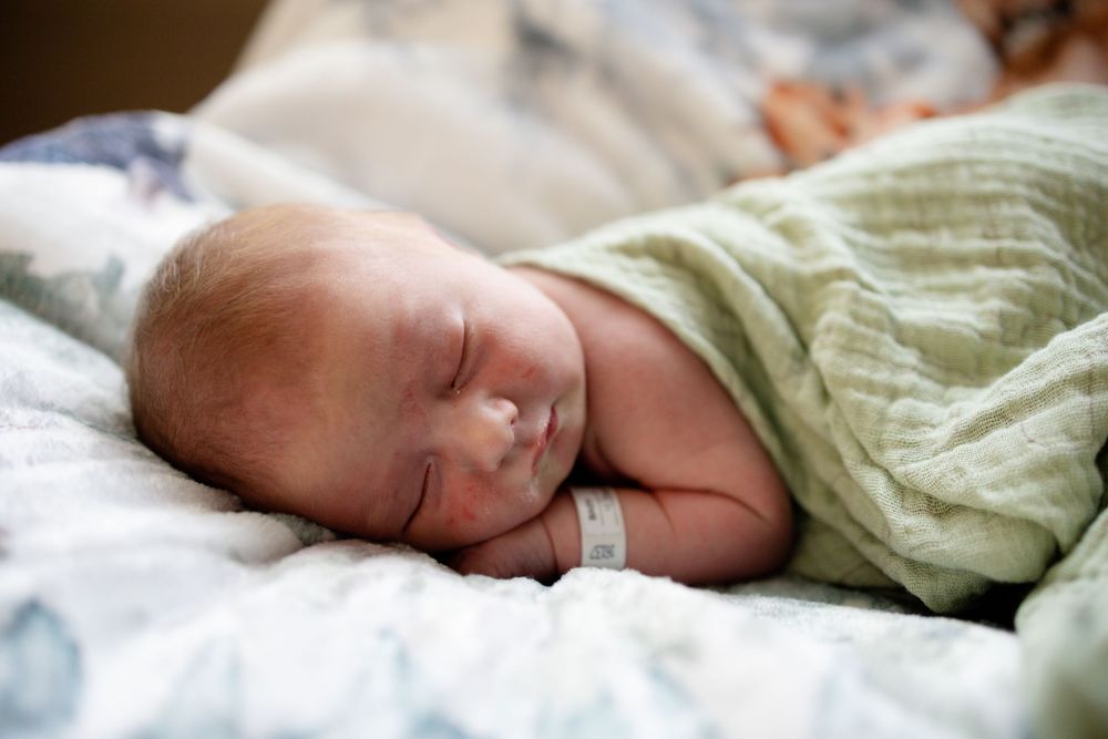 Peaceful newborn baby sleeping on white blanket wrapped in soft green swaddle cloth.