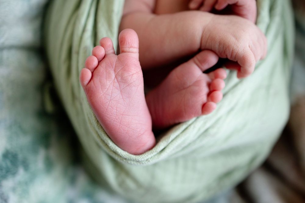 Close-up of newborn baby tiny feet wrapped in a soft green swaddle blanket.