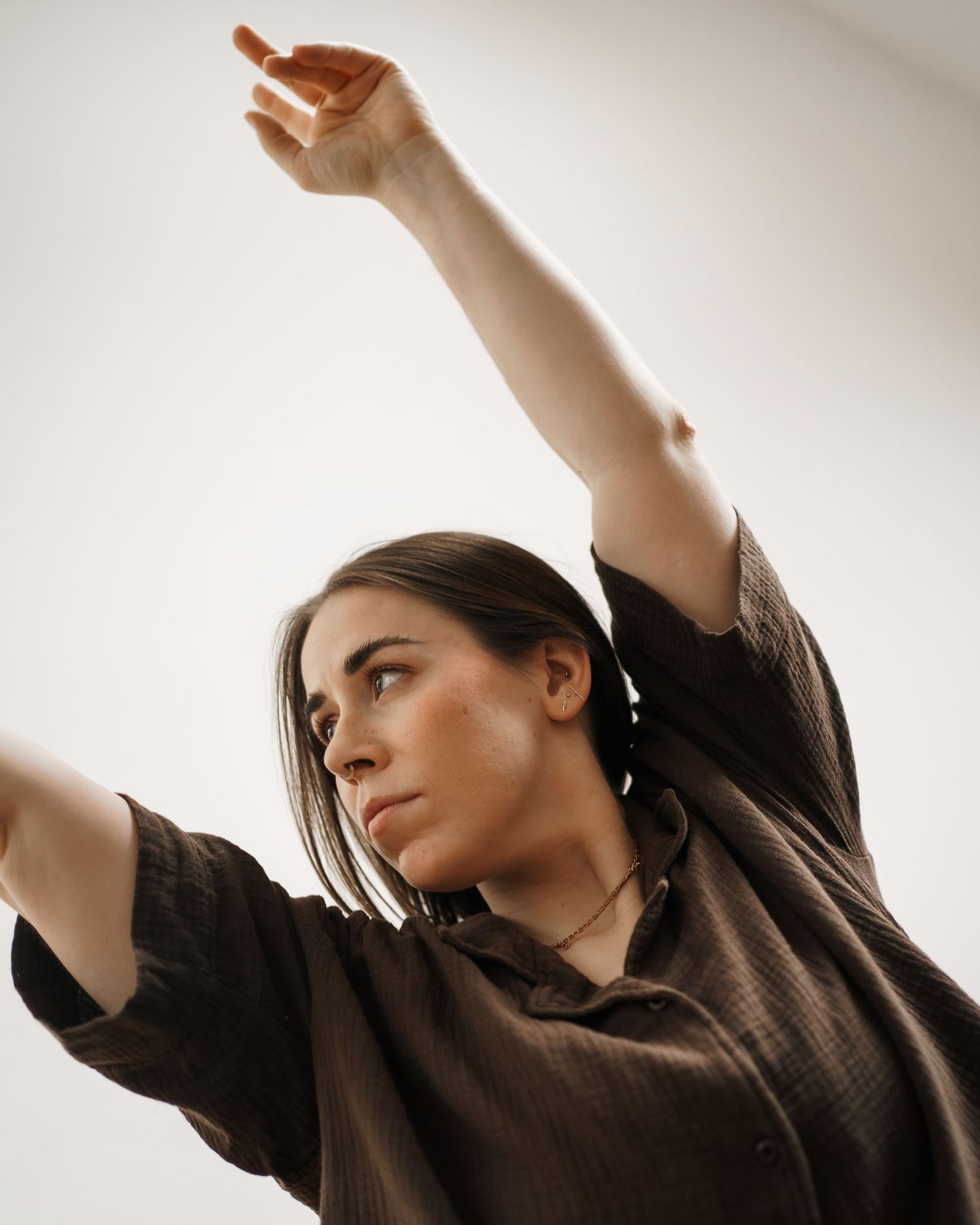 Woman in dark shirt raises arm gracefully against white background in artistic dance pose.