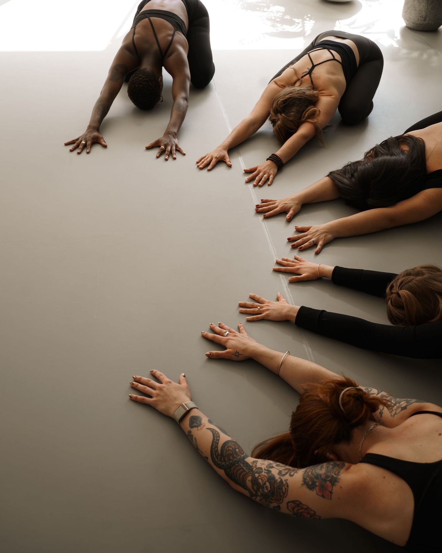 Group of women in black activewear performing a synchronized floor stretch pose in a yoga studio.