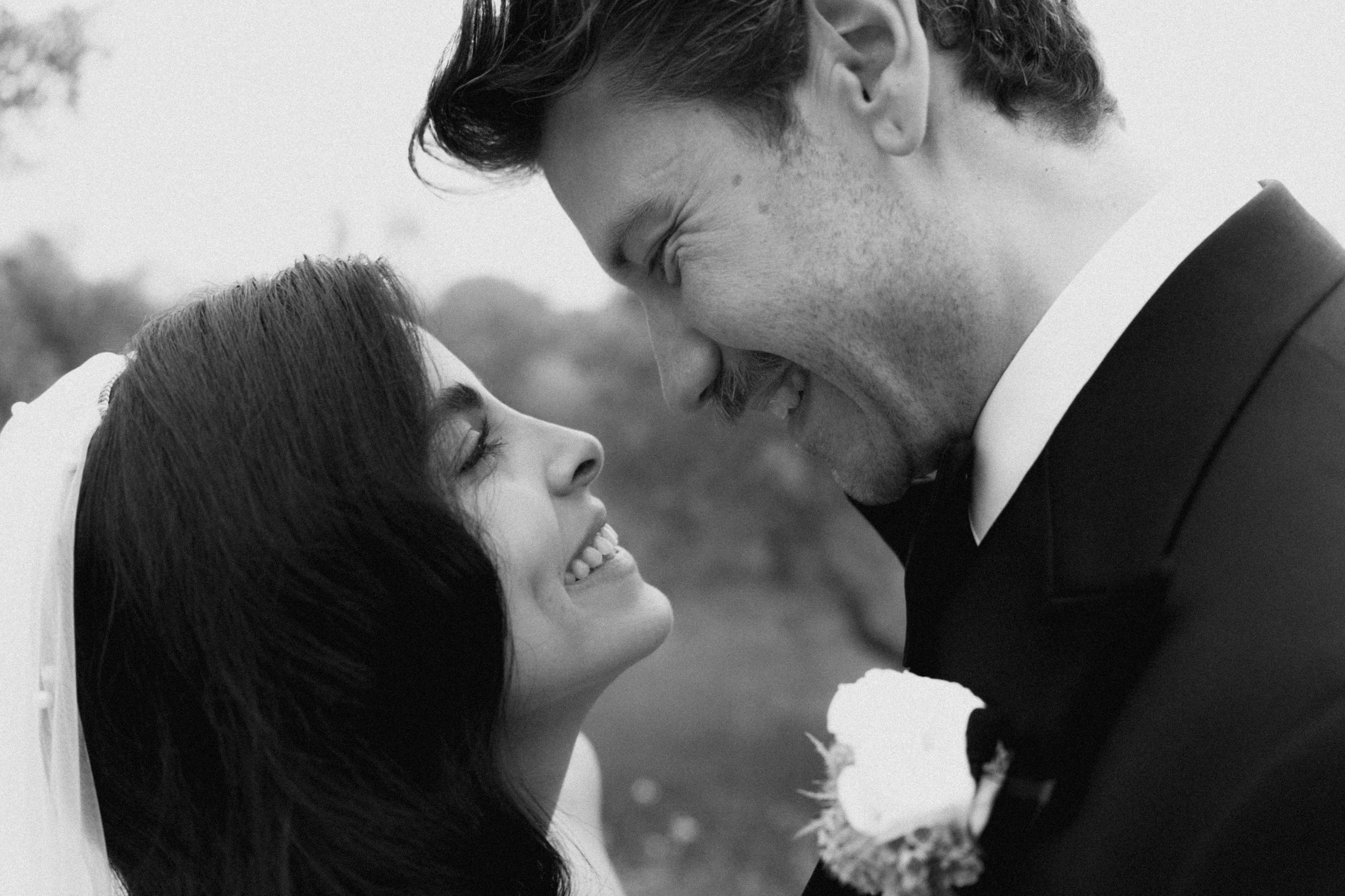 Black and white wedding photo of smiling bride and groom sharing a joyful intimate moment.