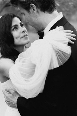 Black and white photo of a bride and groom embracing, the bride gazing up lovingly at the groom in wedding attire.