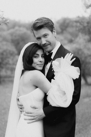 Black and white wedding portrait of bride and groom embracing outdoors, bride in strapless gown with veil.