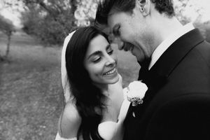 Black and white wedding photo of smiling bride and groom sharing an intimate moment outdoors.
