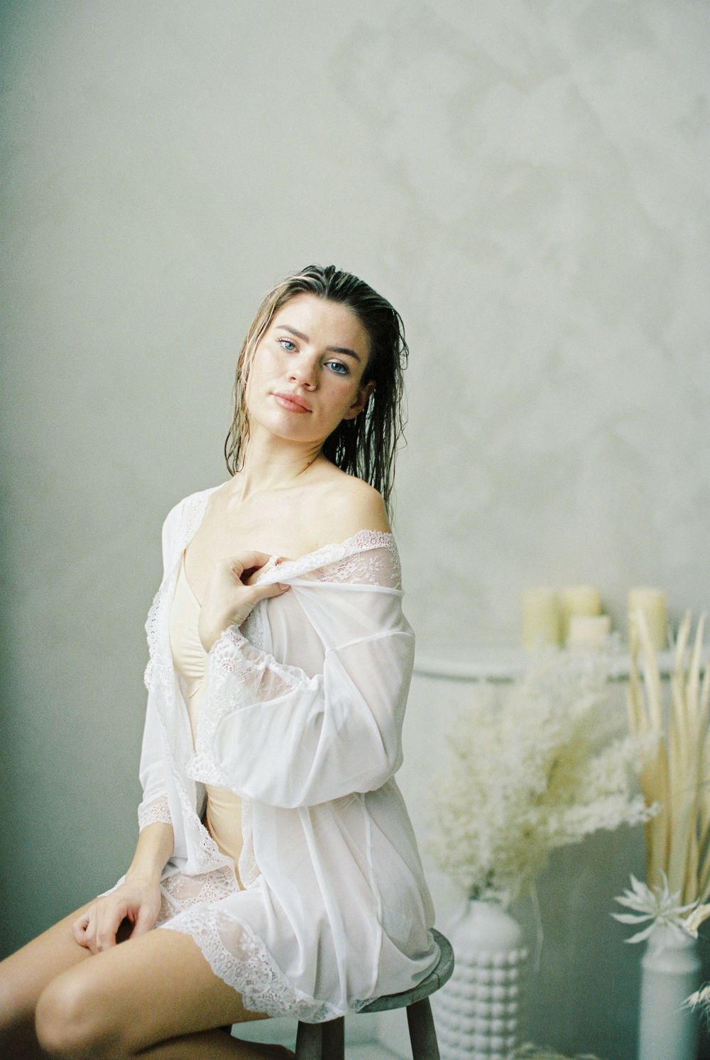 Woman in white sheer lace robe sitting gracefully, wet hair, soft natural light, elegant boudoir photography style.