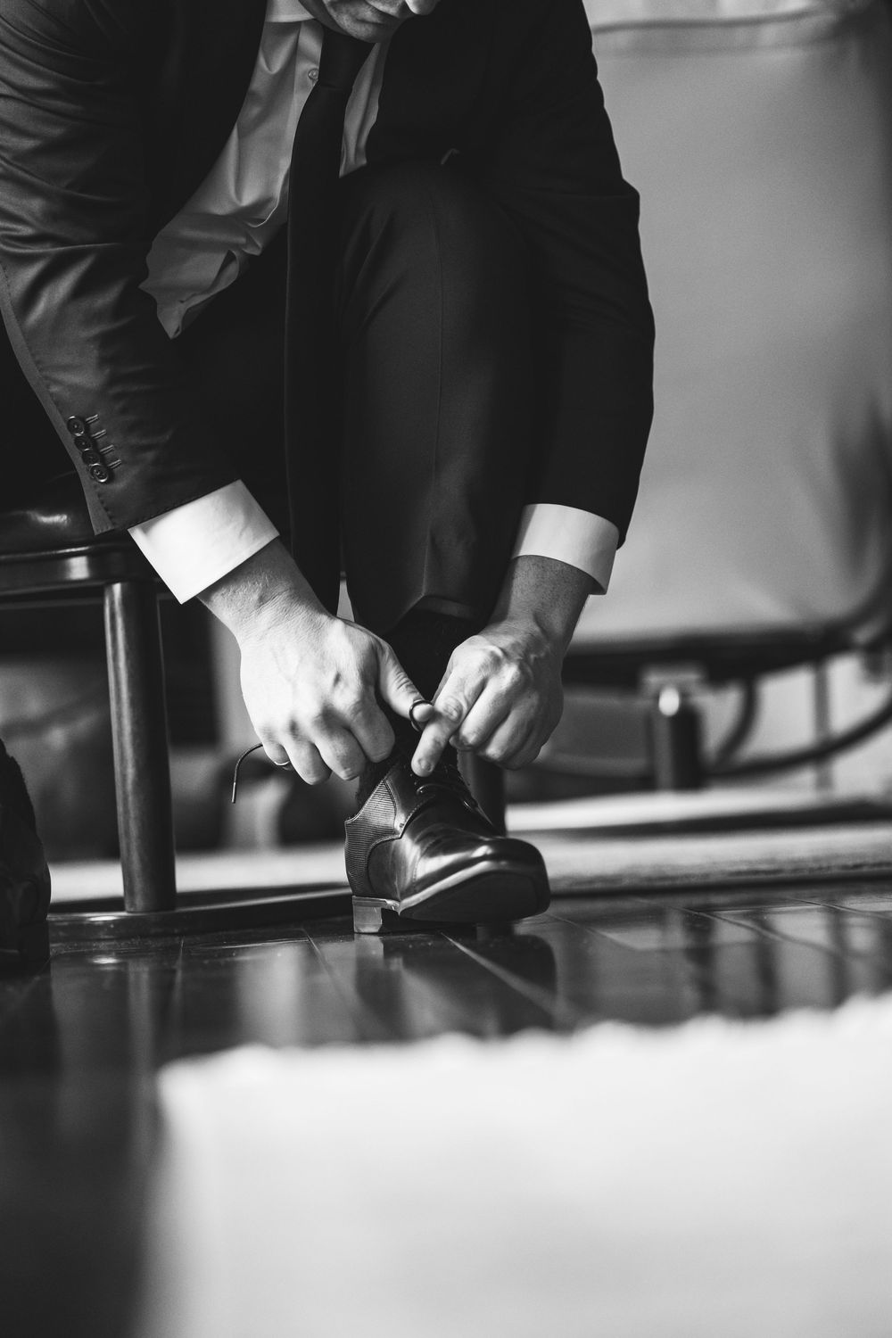 Black and white photo of a man in a suit tying his dress shoes, perfect for wedding or formal event styling.