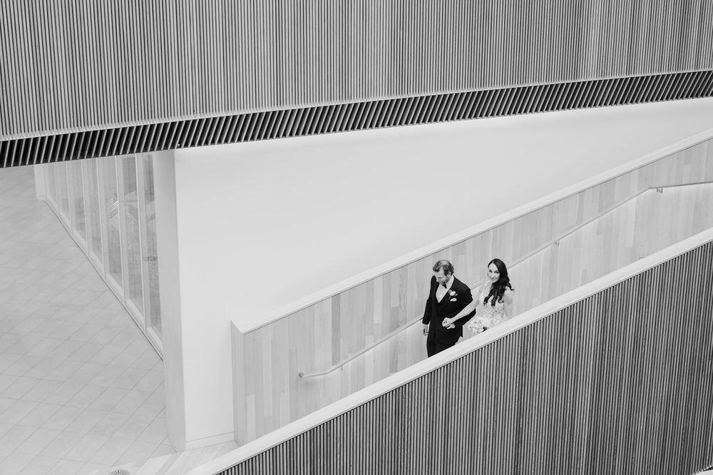 Black and white wedding photo of bride and groom standing on a modern architectural balcony.
