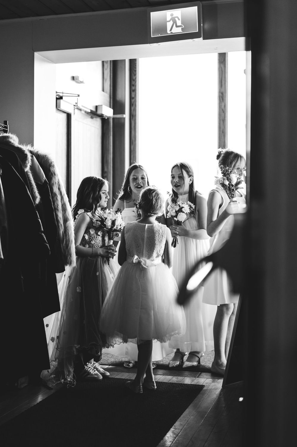Black and white photo of bridesmaids and flower girls gathered in a doorway holding bouquets at a wedding.