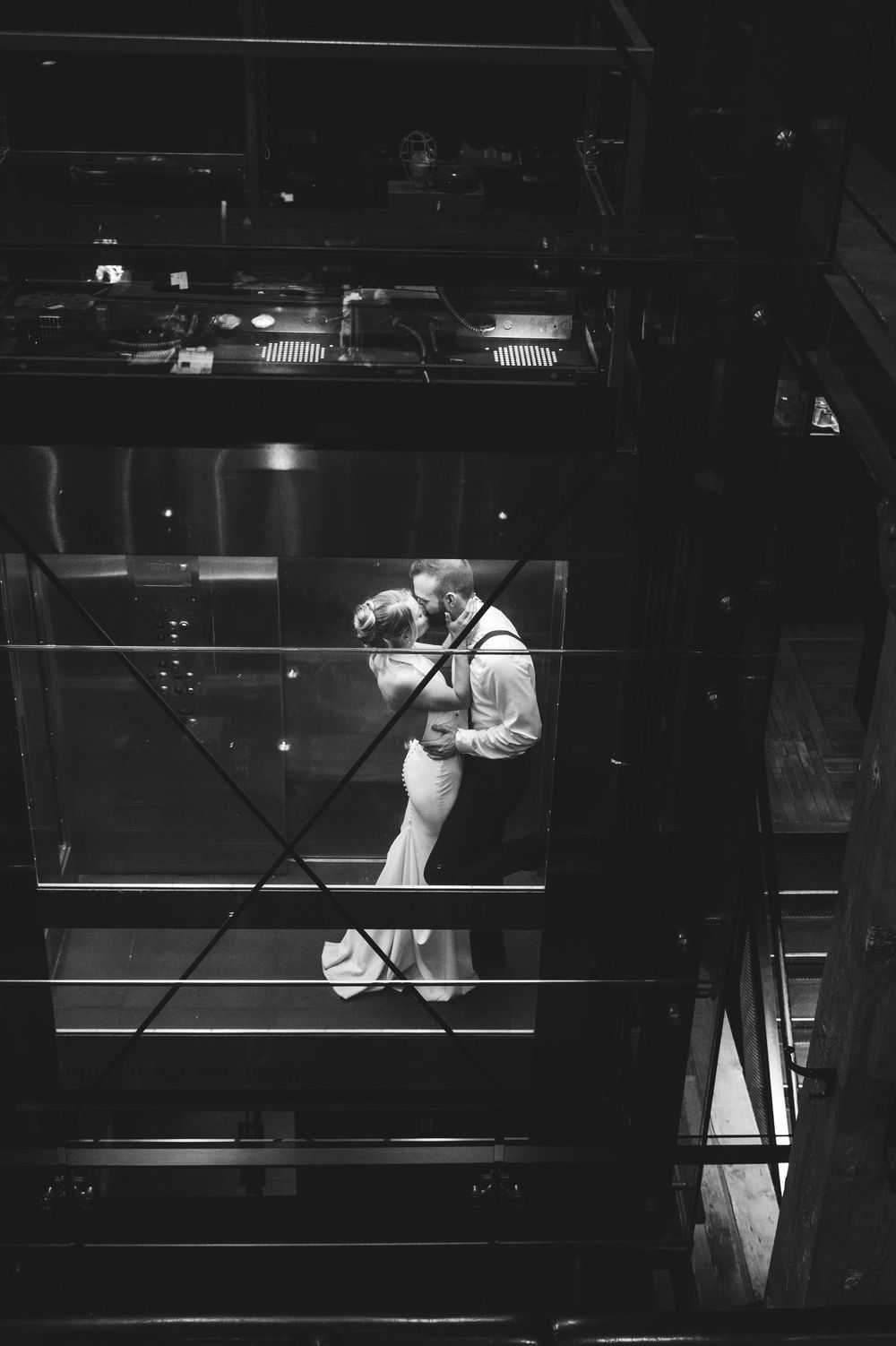 Black and white photo of a couple sharing a romantic kiss on a glass staircase at their wedding reception.