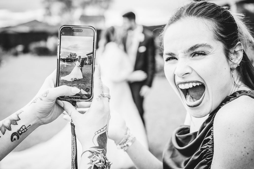 Invitada fotografiando a una pareja durante una boda en Asturias mientras sonríe a cámara.