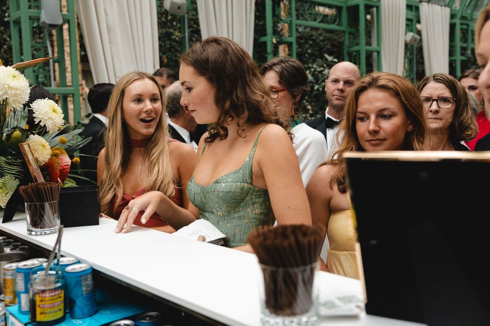 Women smiling and socializing at an elegant indoor event, gathered around a white table with drinks nearby.
