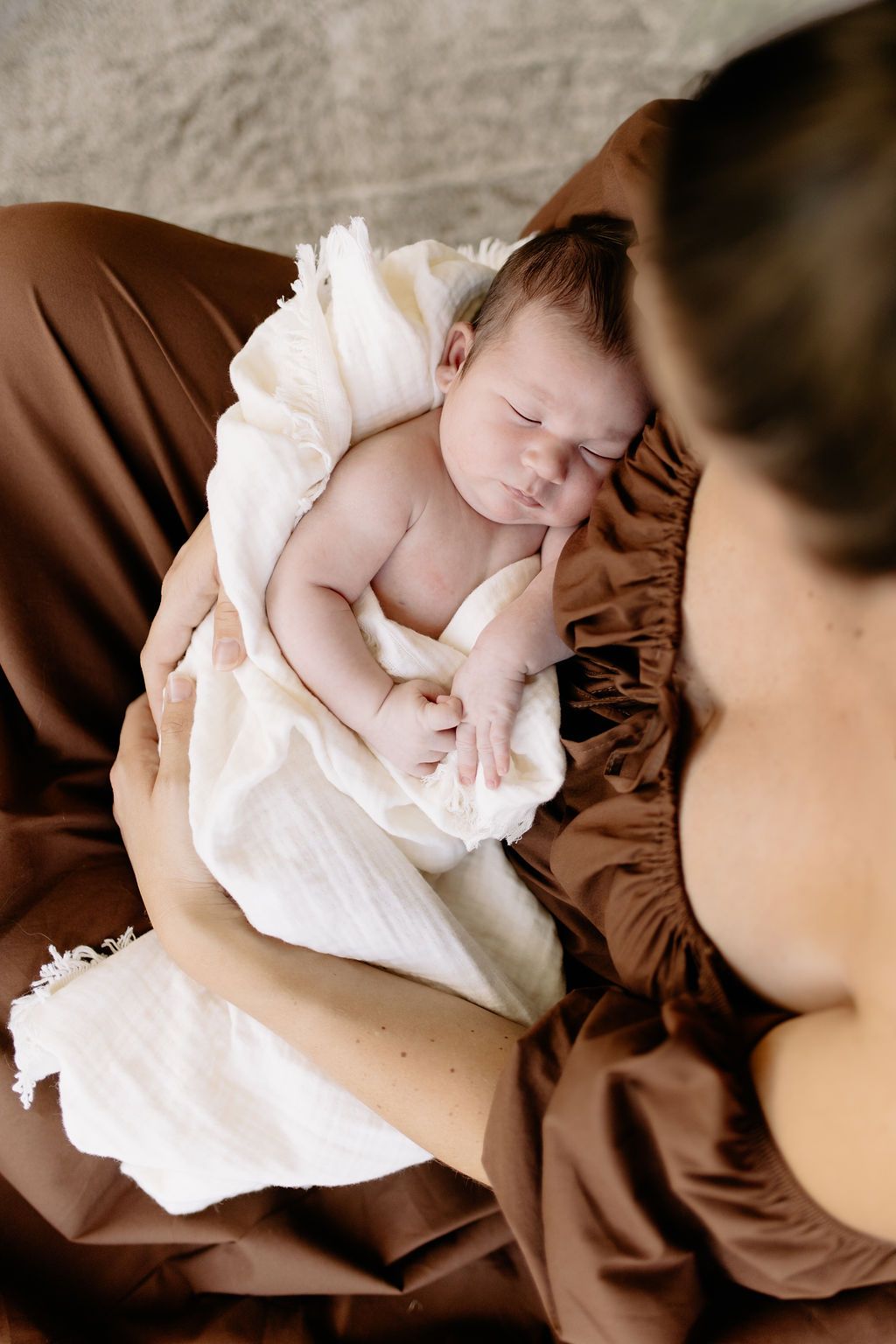 Maman portant une robe marron chocolat qui tient son nouveau-né dans les bras