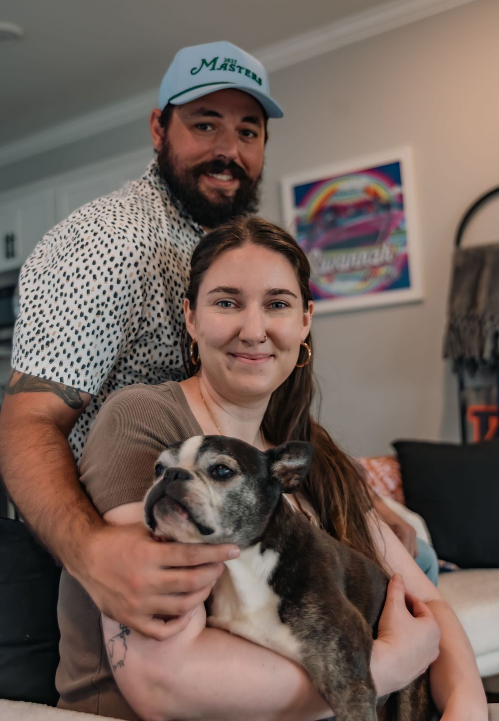 Couple smiling with their French Bulldog in a cozy living room.