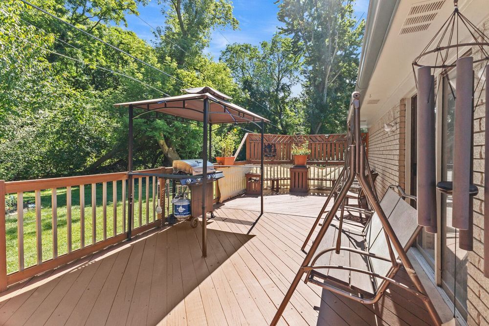 Wooden deck with gazebo, patio furniture, and lush green trees providing privacy in backyard.