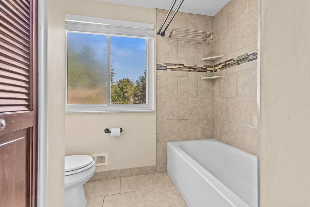 Clean bathroom with tiled shower-tub combo, toilet, tile flooring, and frosted privacy window.