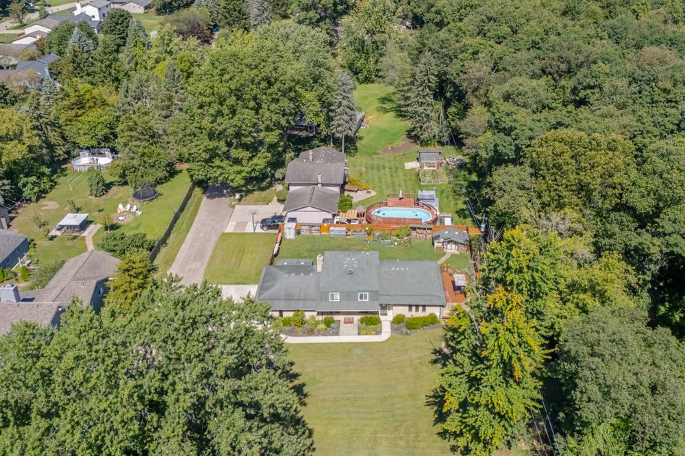 Aerial view of a spacious property with a large home, pool, patio, and lush surrounding trees.