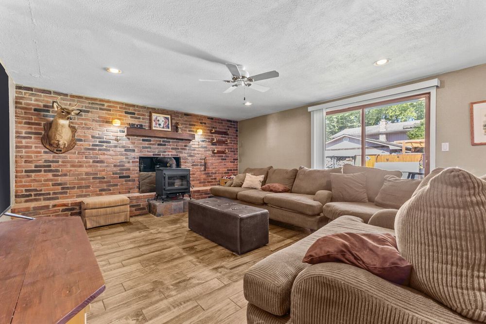 Cozy living room with brick accent wall, wood-burning stove, hardwood floors, and large sectional sofa.