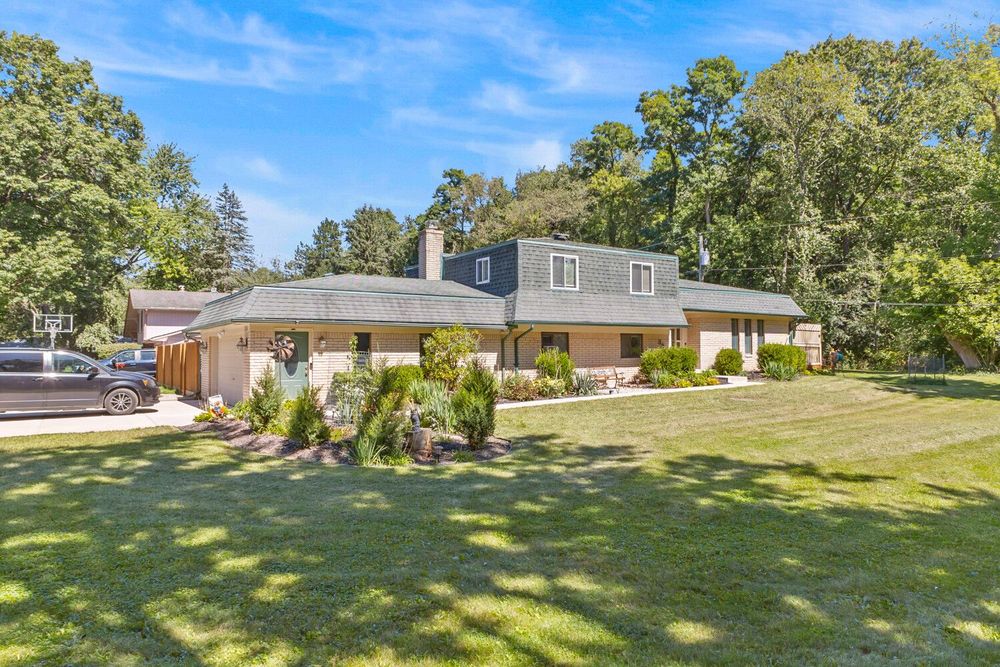 Large brick and wood ranch home with expansive green lawn, mature trees, and well-kept landscaping.