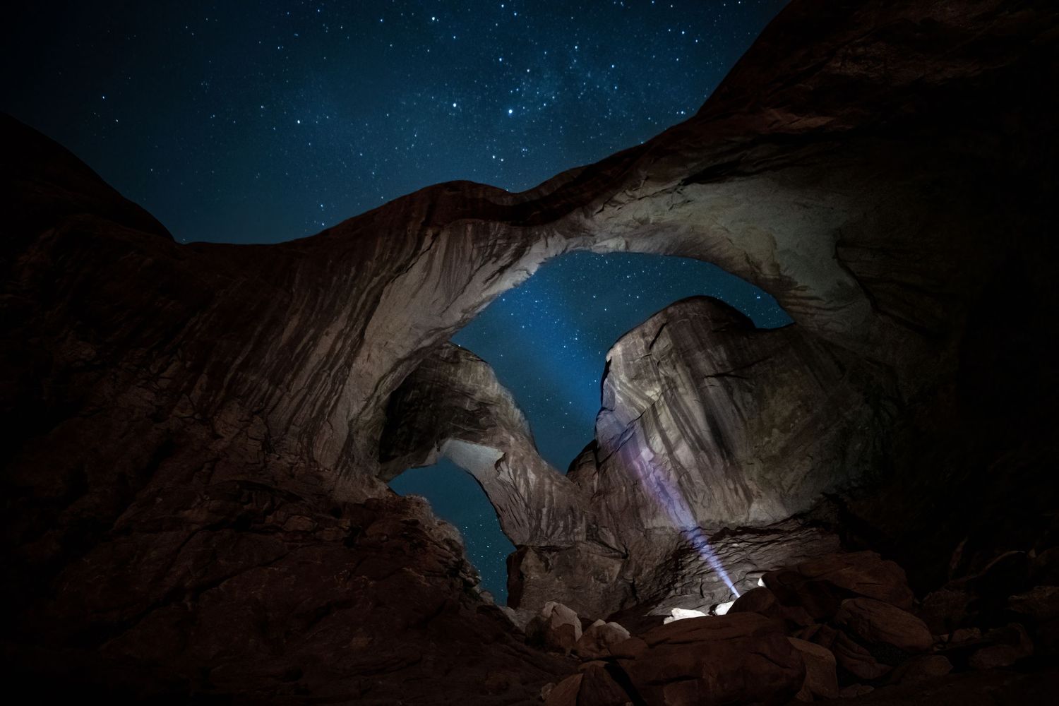 Starry night sky viewed through Double Arch rock formation in Arches National Park with flashlight beam.