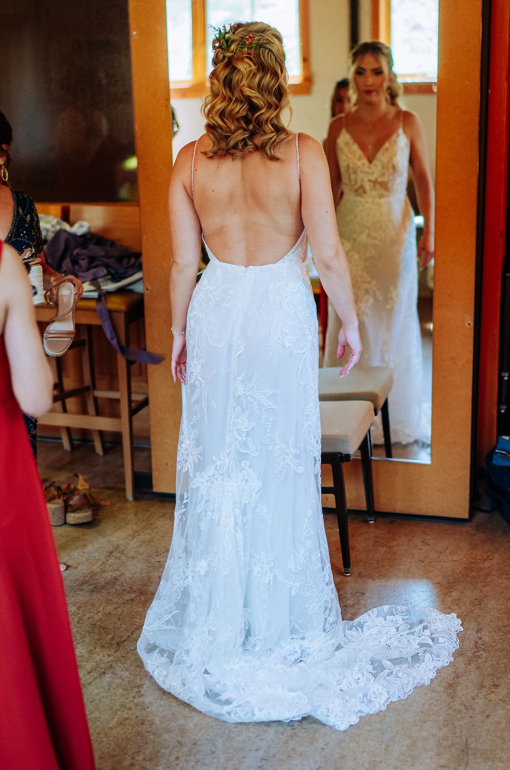 Bride in backless lace wedding gown with train, viewed from behind, reflected in mirror.
