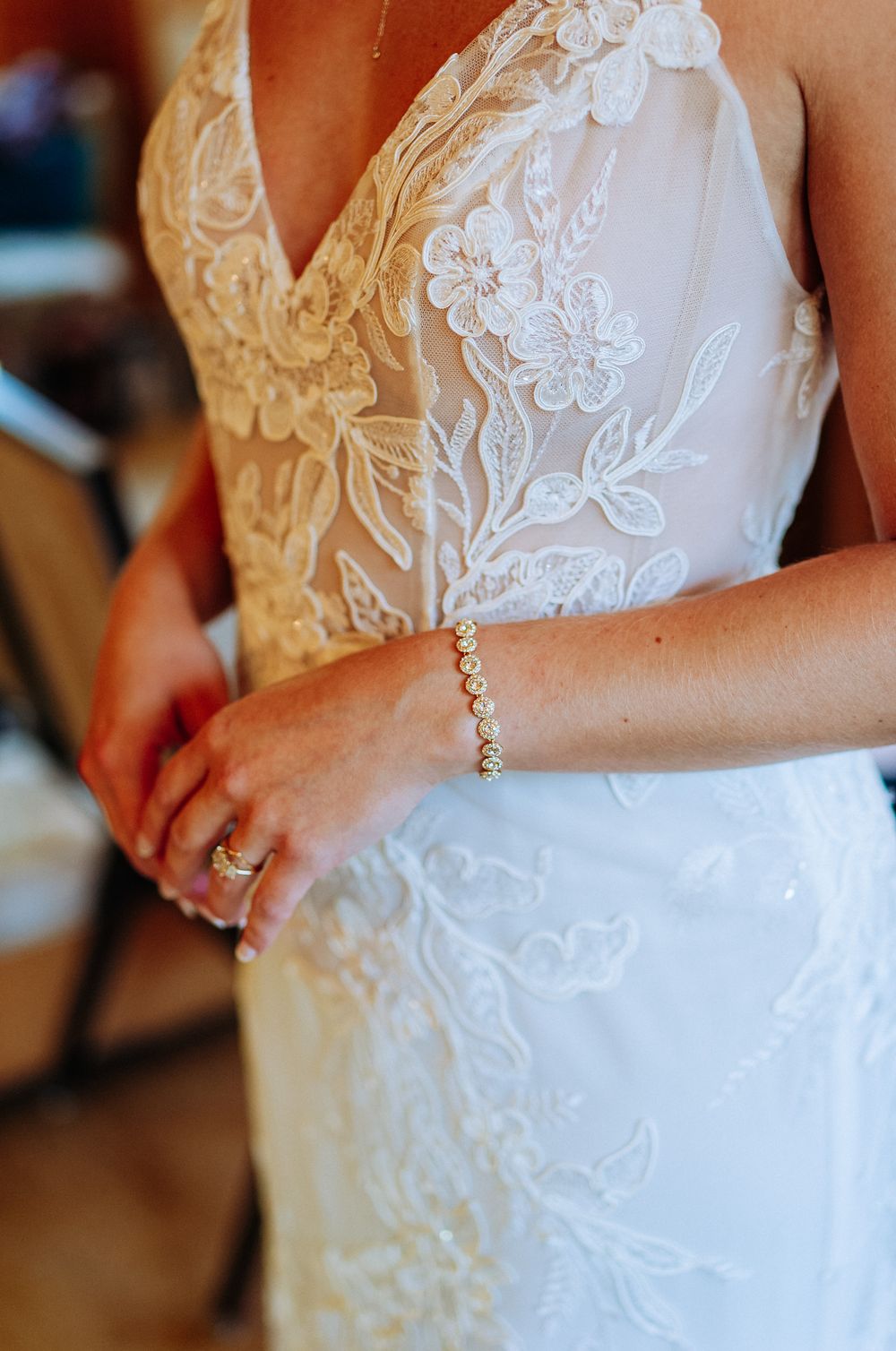 Bride in lace wedding gown with floral embroidery, wearing a gold bracelet and engagement ring.