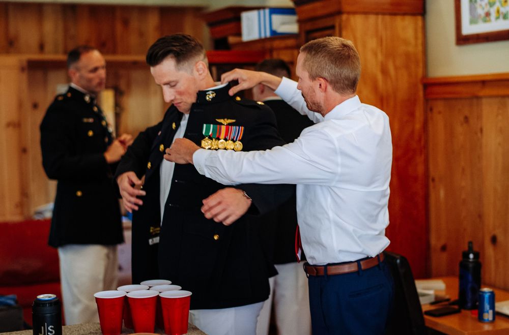 Man in Marine dress uniform getting medals adjusted by another man in a wood-paneled room with red Solo cups.