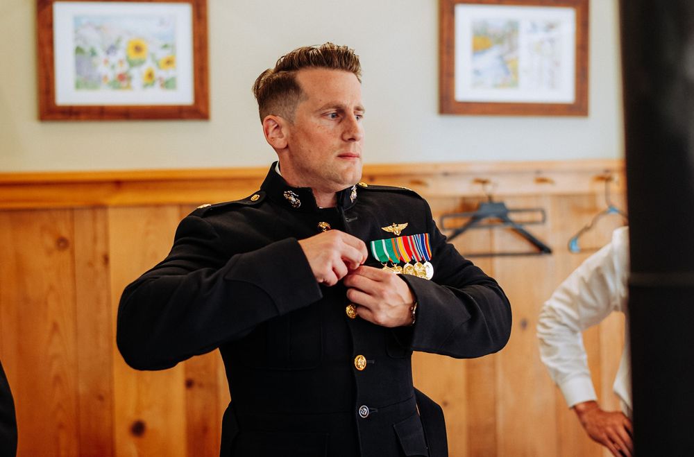 Military officer in dress uniform adjusting service medals and ribbons indoors at a formal ceremony.
