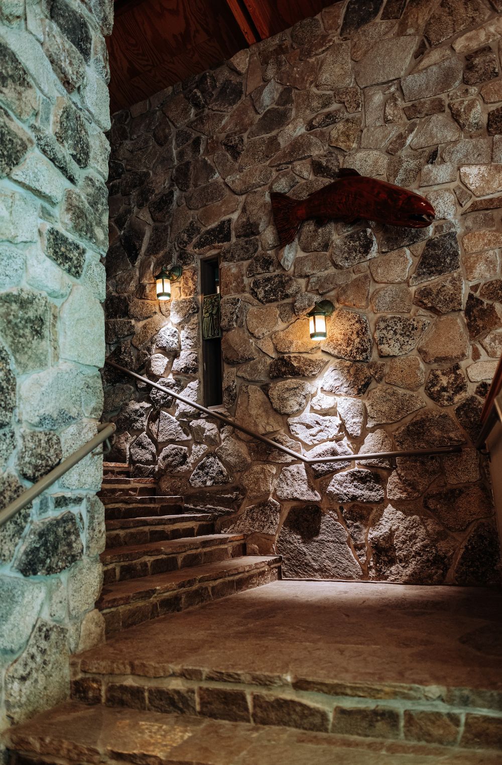 Stone staircase with rustic rock walls and vintage wall lanterns creating a warm, medieval-inspired interior ambiance.