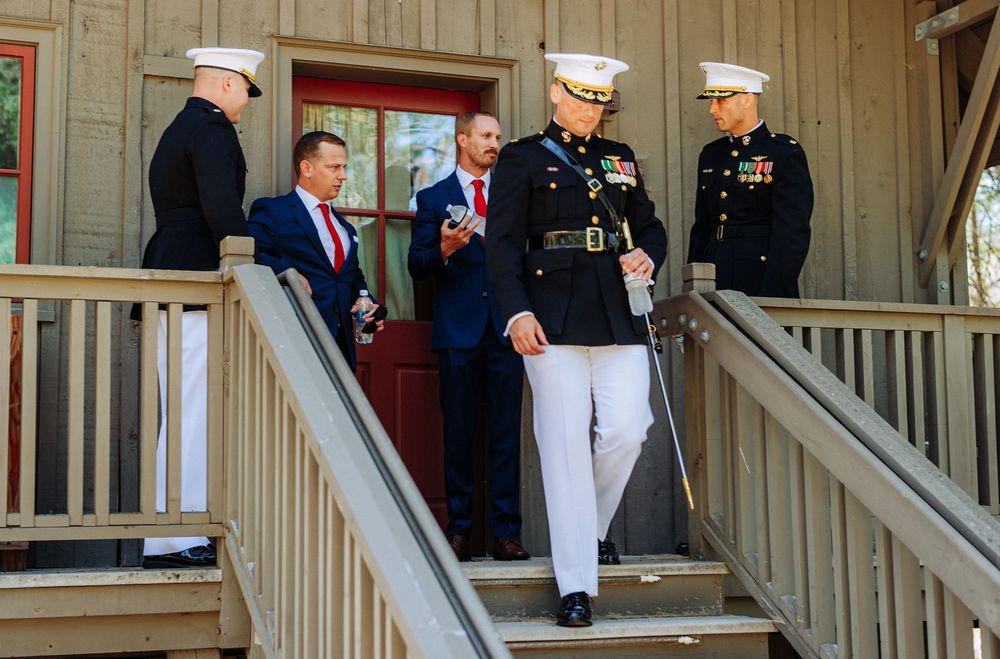 Marines in dress uniforms stand on wooden steps with men in suits during an outdoor military ceremony.