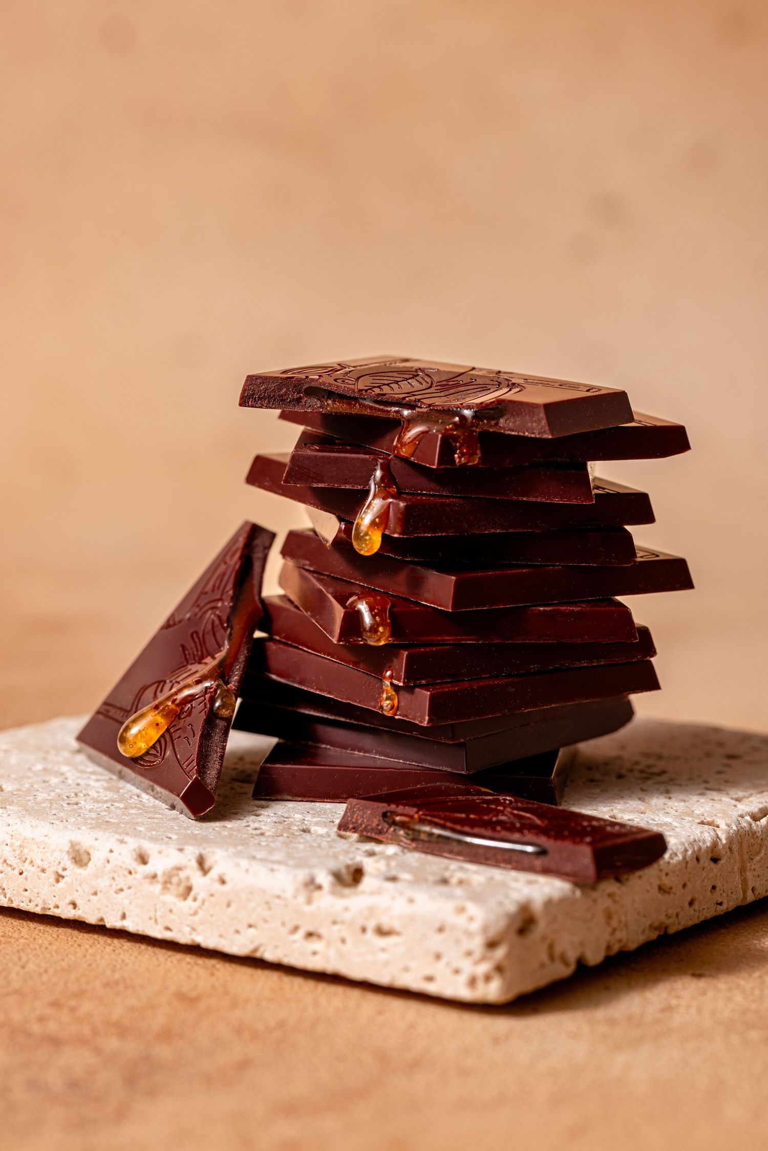 Stacked pieces of dark chocolate arranged on a light textured surface in warm lighting.