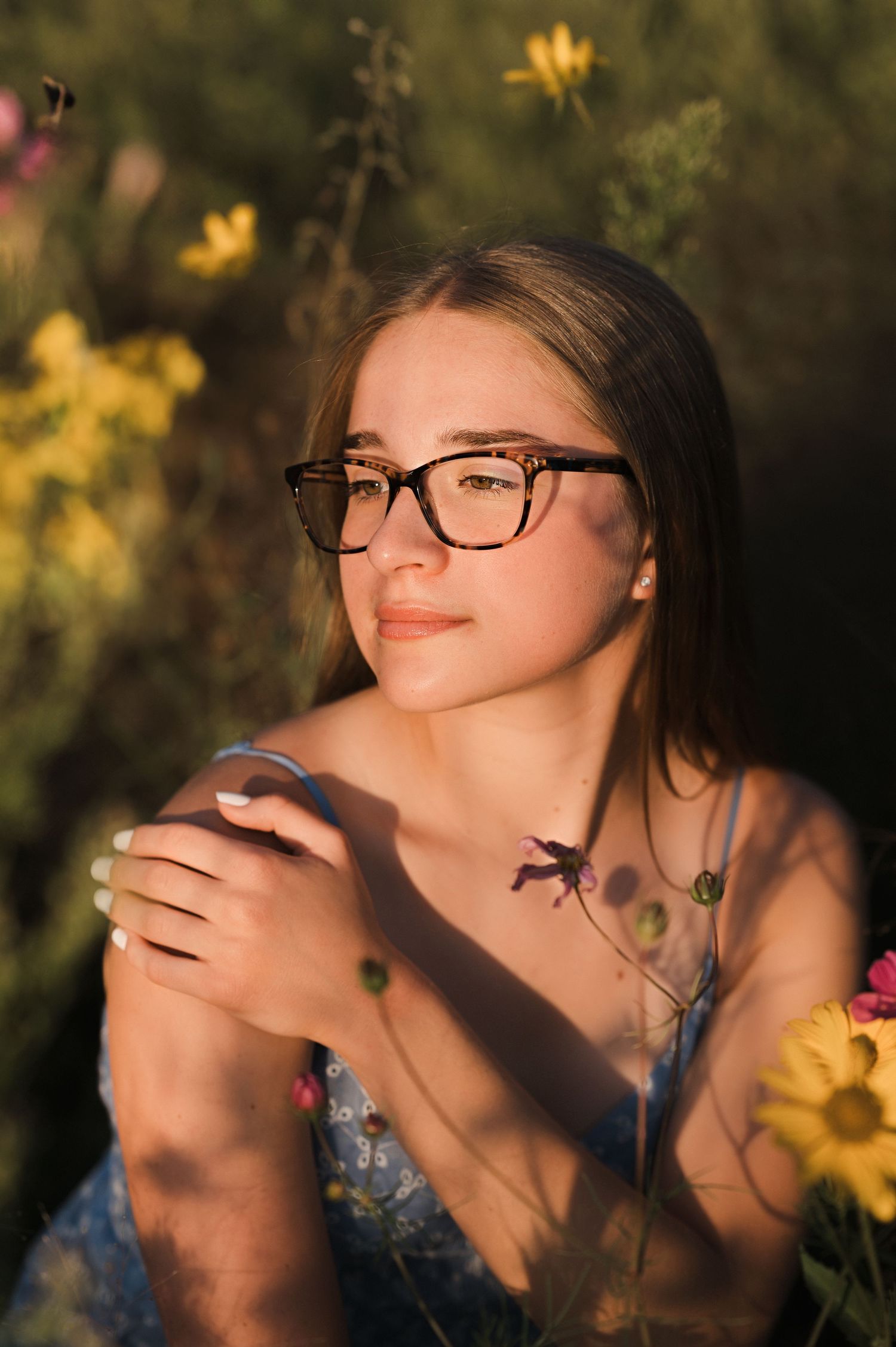 Senior girl portrait with glasses photographed outdoors in warm golden light with lush greenery and a soft timeless edit.