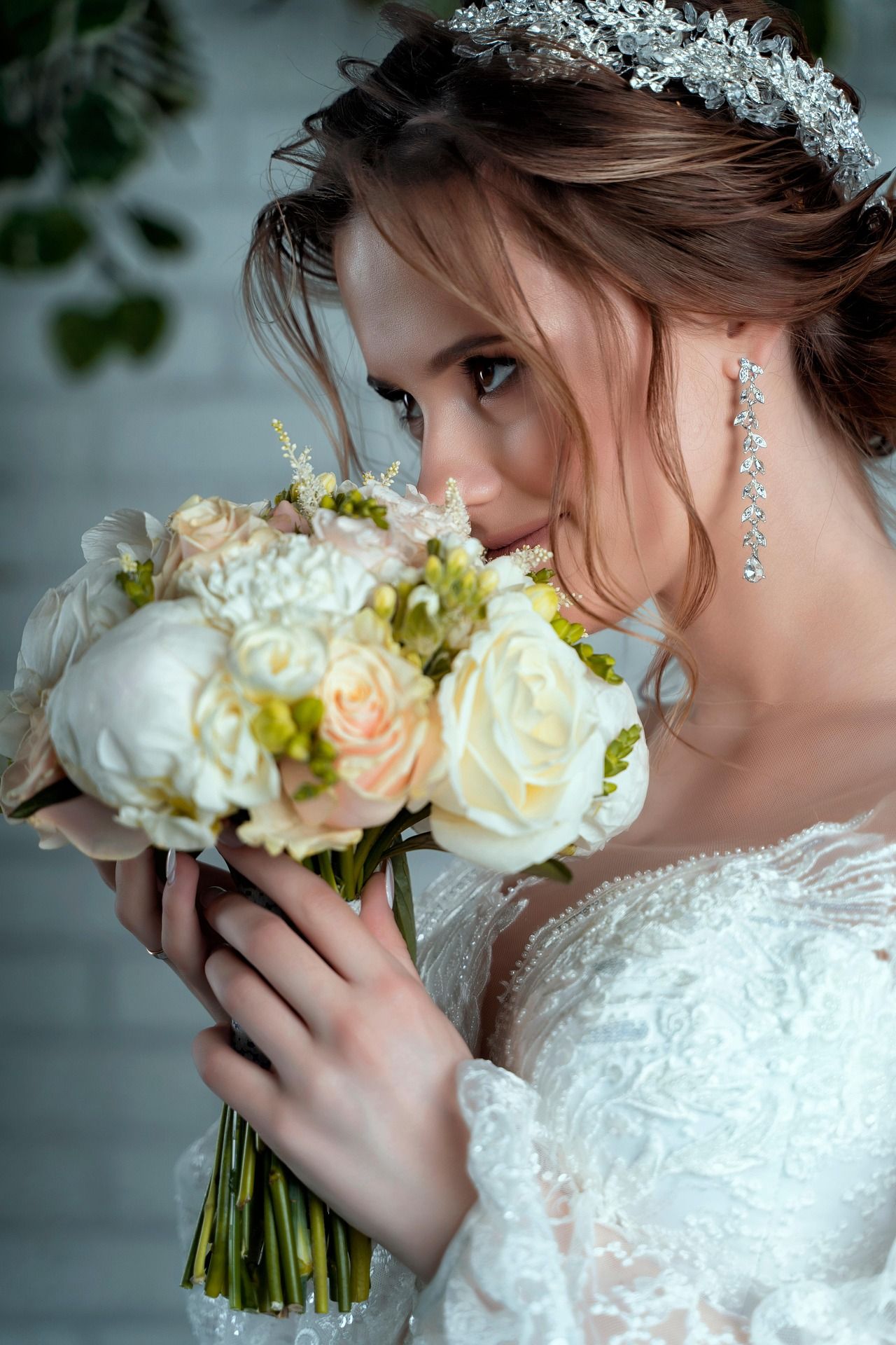 Beautiful bride in white lace gown and crystal tiara smelling her bouquet of white and blush roses.