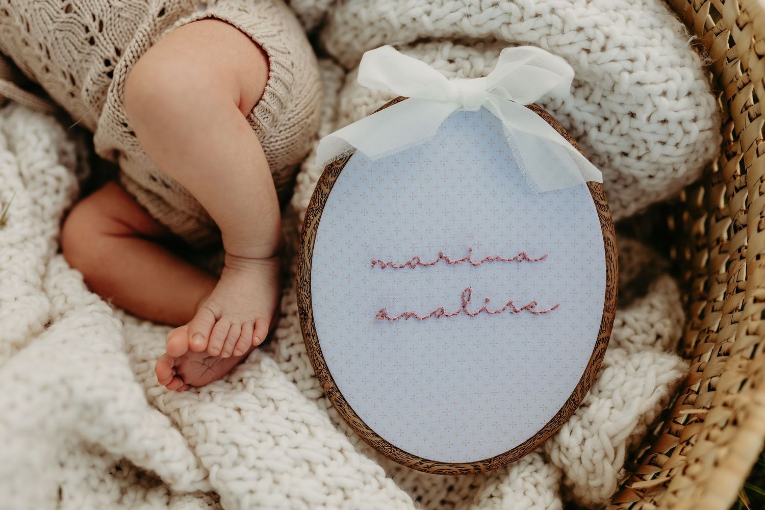 Newborn baby feet beside embroidered hoop sign reading Marina Analise in a cozy knit basket.