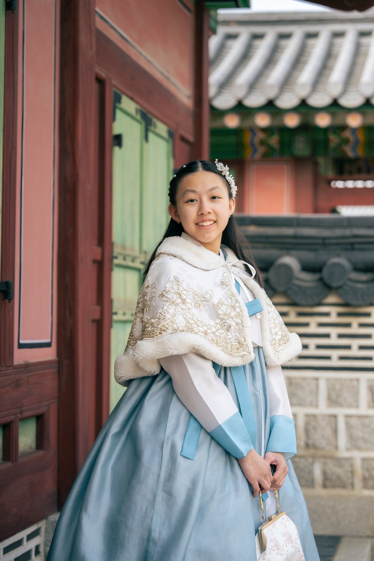 Young woman smiling in traditional Korean hanbok dress with white embroidered cape at historic palace.