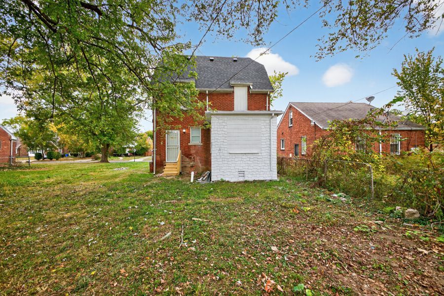 Brick two-story home with white garage door, lush green lawn, and mature trees in a residential neighborhood.