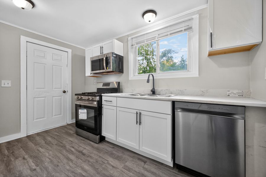 Modern kitchen with white cabinets, stainless steel appliances, dark hardwood floors, and a window above the sink.