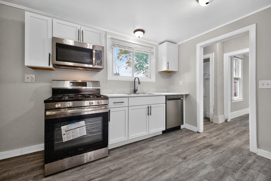 Modern kitchen with white cabinets, stainless steel appliances, gas range, and hardwood floors in a bright renovated home.