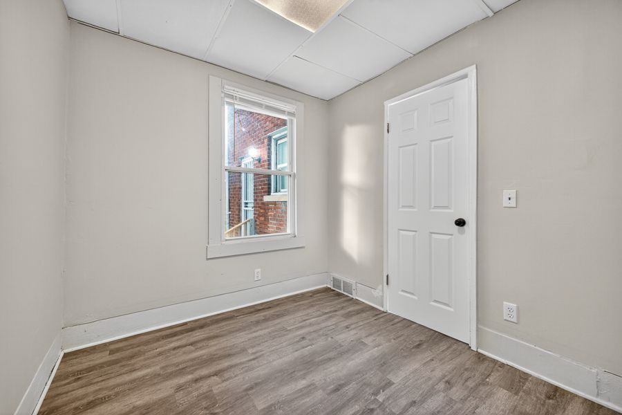 Empty room with light wood floors, white trim, a window, and a white six-panel door in a freshly renovated home.