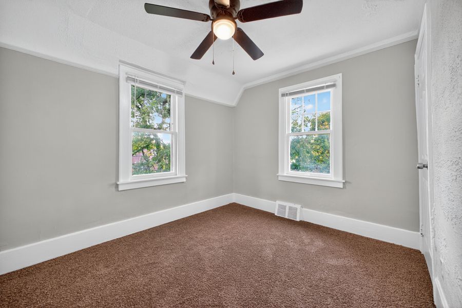 Carpeted bedroom with ceiling fan, crown molding, and two bright windows with green outdoor views.