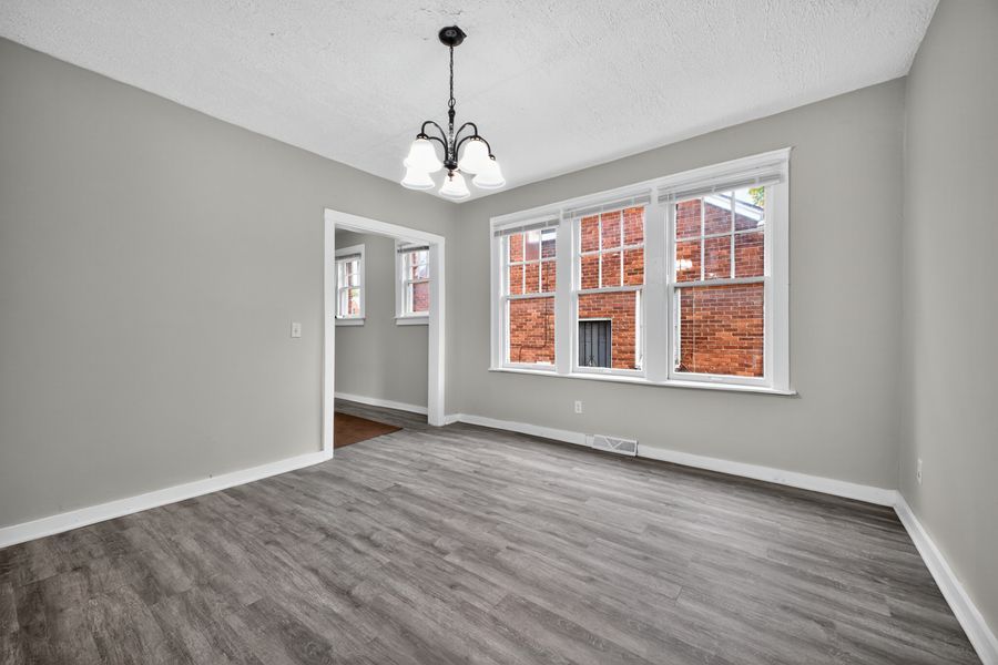 Bright dining room with hardwood floors, gray walls, chandelier, and large windows with brick exterior view.