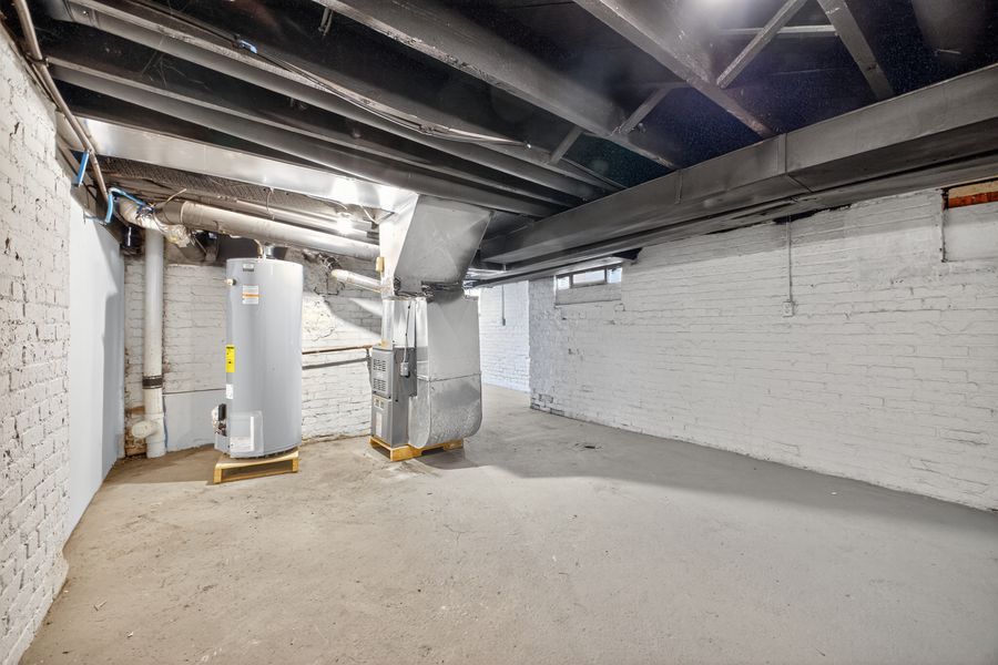 Unfinished basement with exposed beams, brick walls, water heater, and HVAC system on concrete floor.
