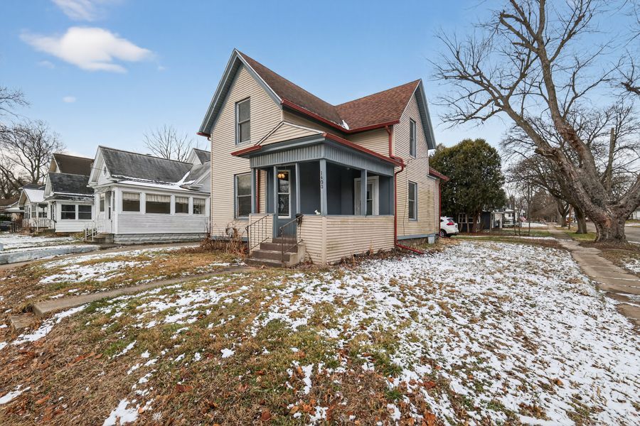 Charming two-story home with a covered front porch, light siding, and a dusting of snow on the front yard.