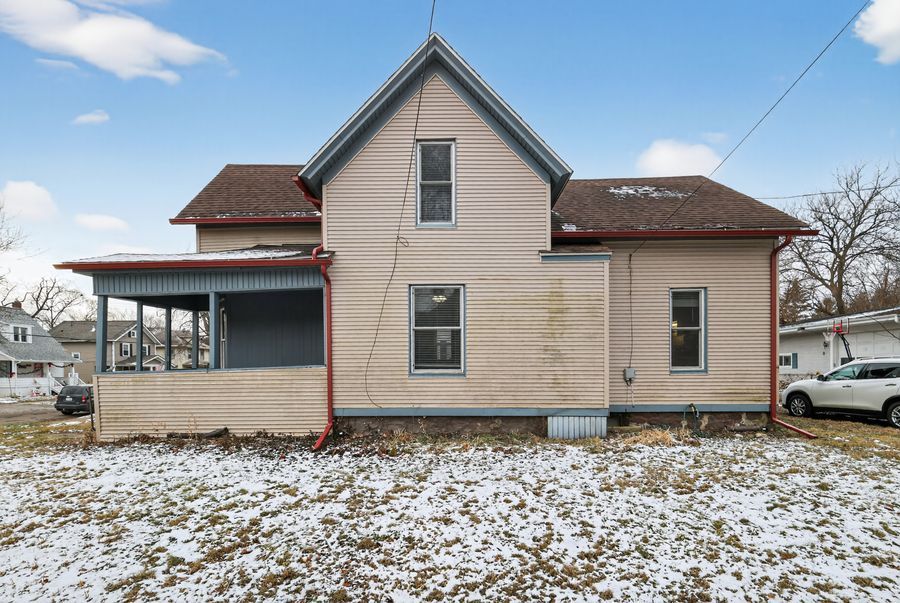 Rear exterior view of a two-story home with pink siding, enclosed porch, and snow-covered yard on a cloudy winter day.