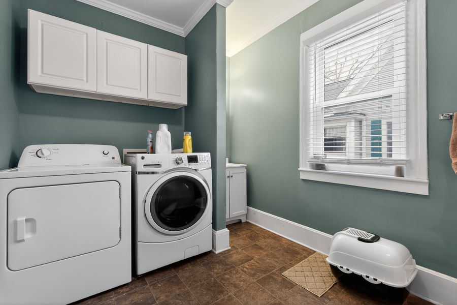 Laundry room with white washer and dryer, teal walls, white cabinets, and a bright window with natural light.