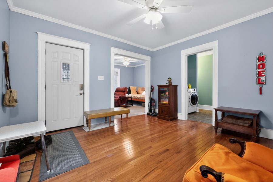 Bright entryway with hardwood floors, blue-gray walls, crown molding, ceiling fan, and white panel door.