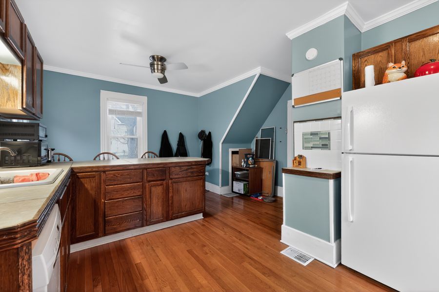 Kitchen with dark wood cabinets, hardwood floors, white refrigerator, and blue walls with crown molding.