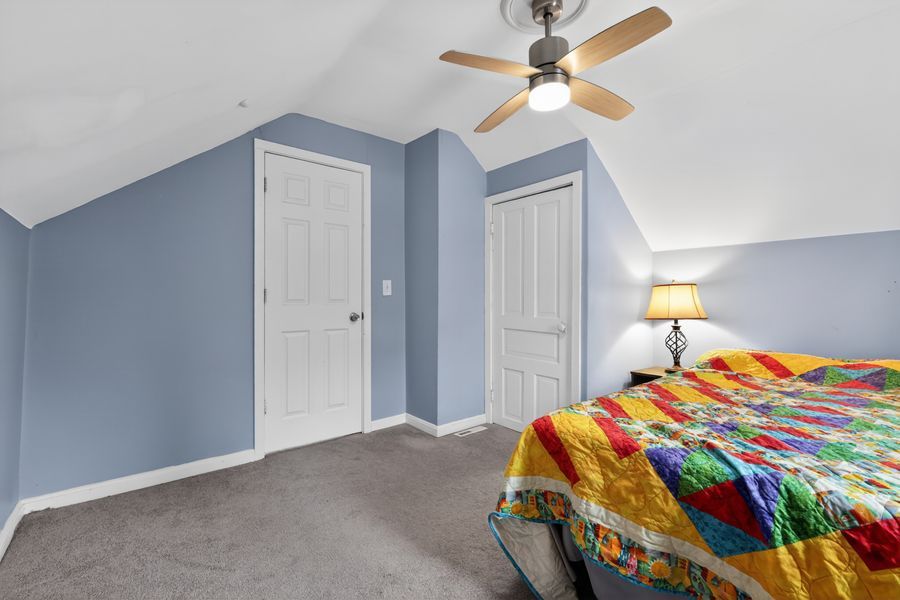 Blue-walled bedroom with vaulted ceiling, ceiling fan, colorful quilt bed, and two white doors on carpet.